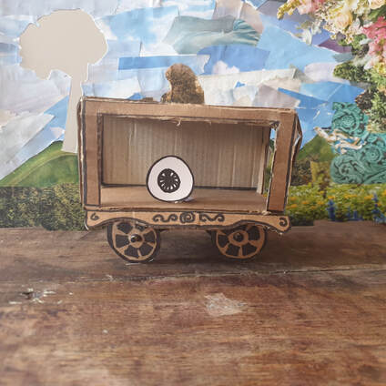 Model cardboard waggon with a paper eye, against a collage of a garden.